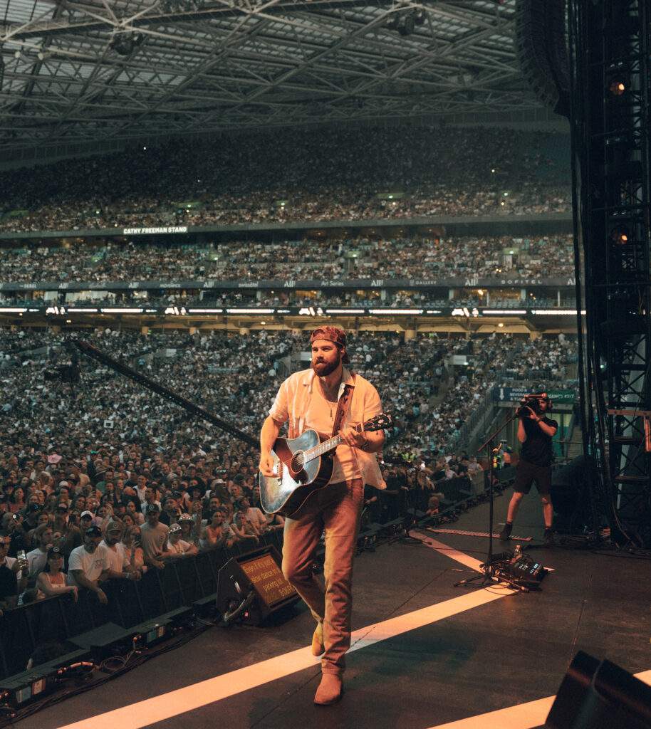 Jordan Davis playing guitar on stage at a stadium show