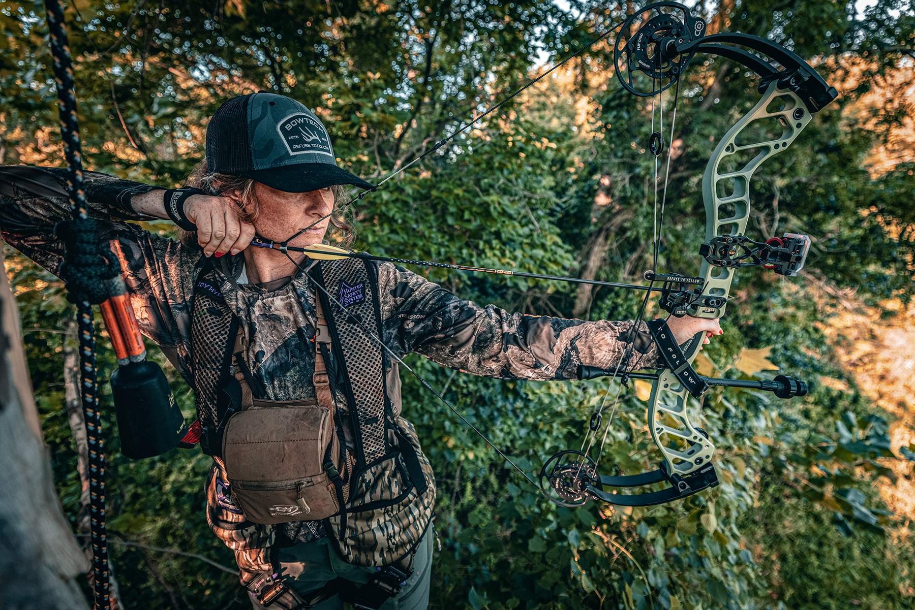 a female hunter in a treestand with the Bowtech Ascend at full draw