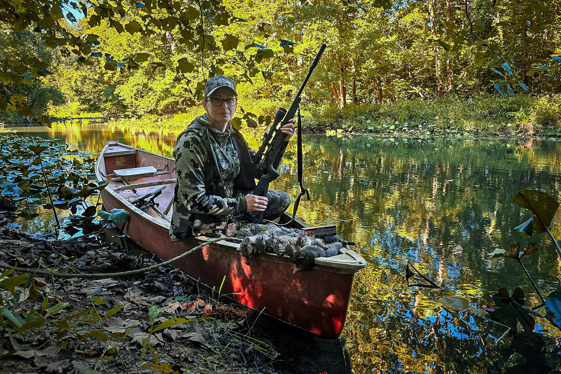 a hunter with a rifle in a canoe with dead squirrels