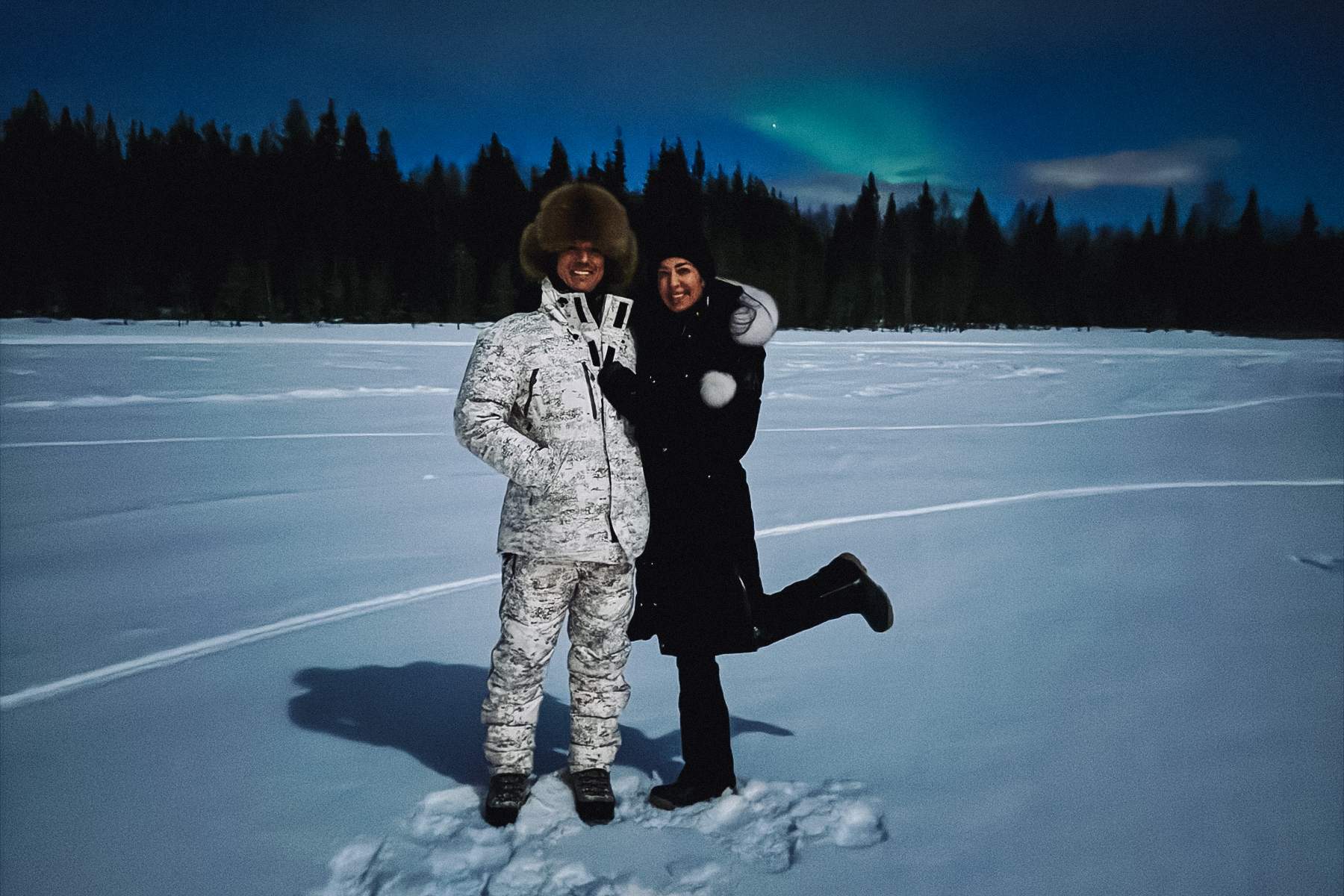 two people standing in the snow with an aurora in the background